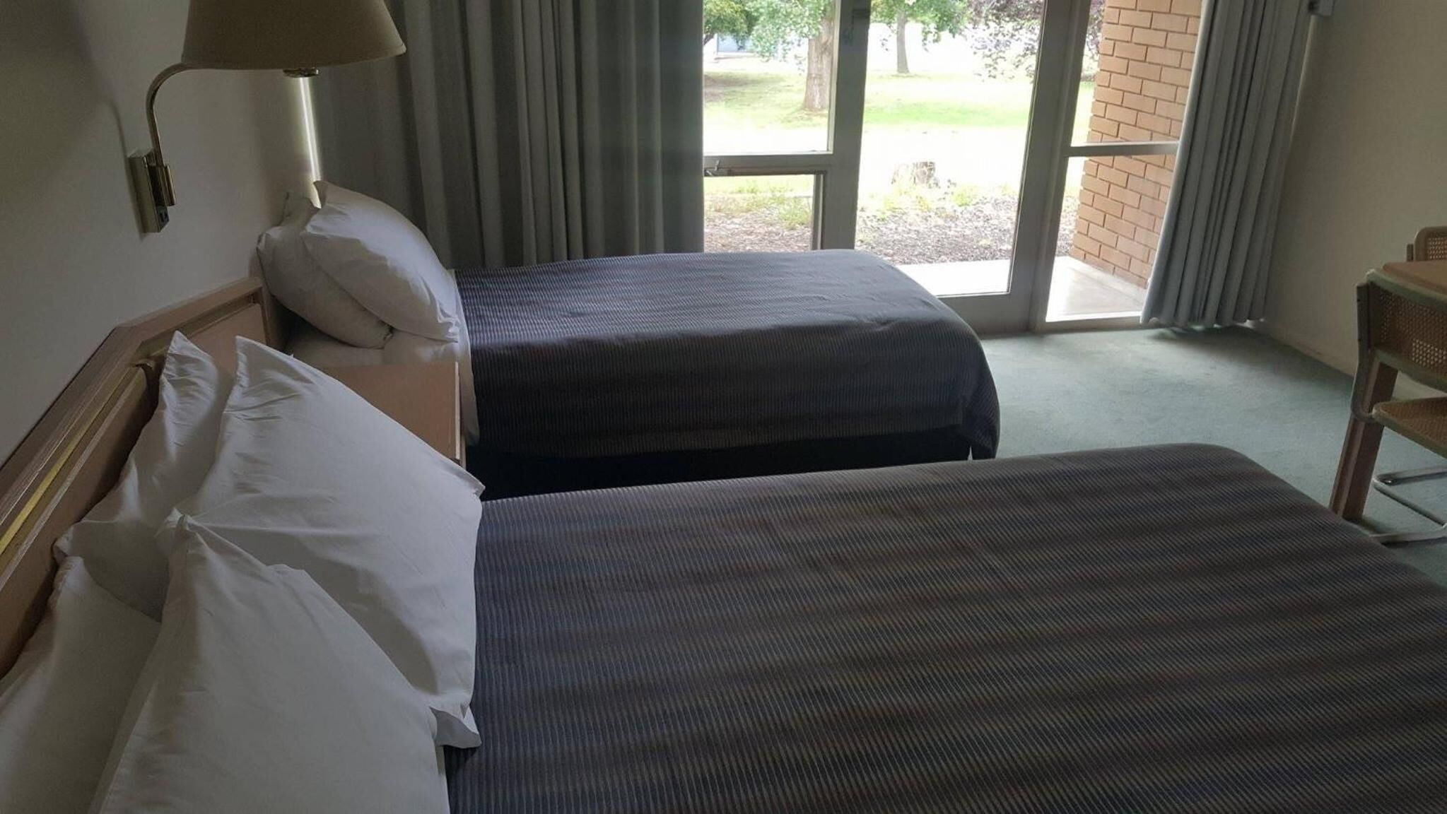 A hotel room with two beds, a lamp, and a view of the outdoors.