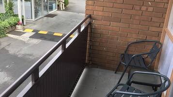 A balcony with a brick wall, a metal railing, and two metal chairs.