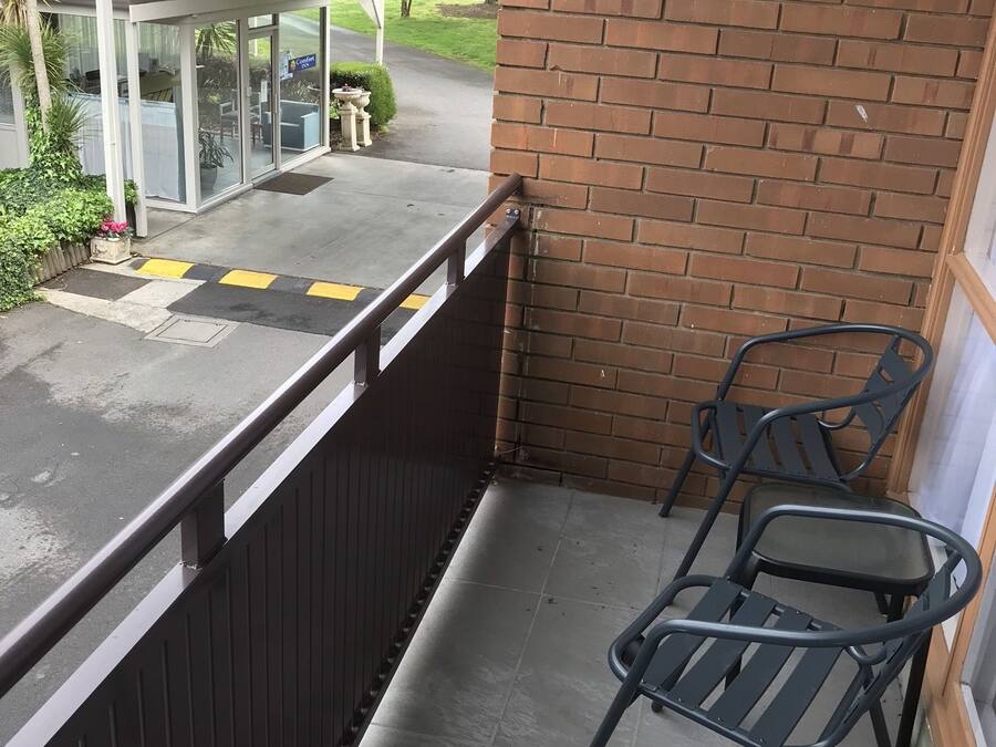 A balcony with a brick wall, a metal railing, and two metal chairs.