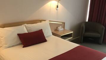 Een hotelkamer met een net opgemaakt bed, een bedlampje, een nachtkastje en een stoel.