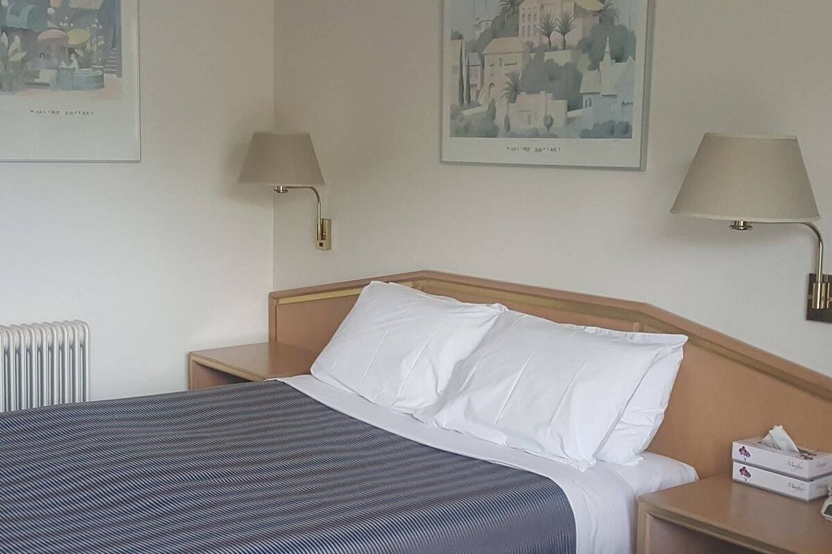 Ein Hotelzimmer mit einem Bett, zwei Nachttischlampen, einer Heizung und zwei gerahmten Bildern an der Wand.