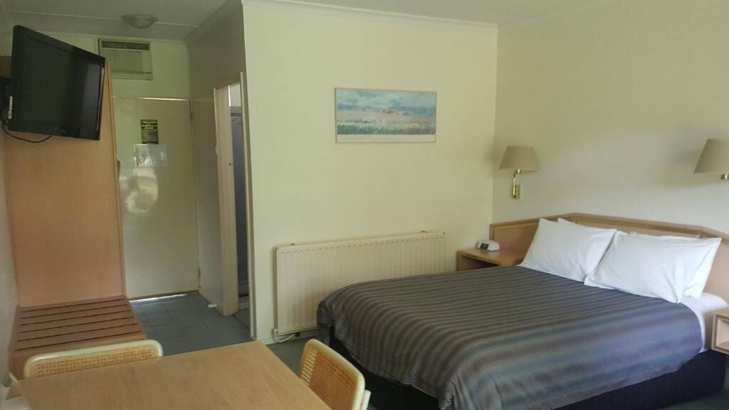 Habitación de hotel con cama, escritorio, silla, televisor, un cuadro en la pared y una lámpara.
