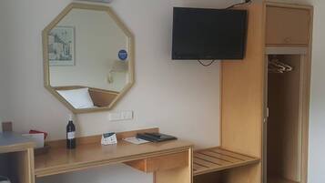 A hotel room with a wooden desk, a mirror, a television, and a wardrobe.