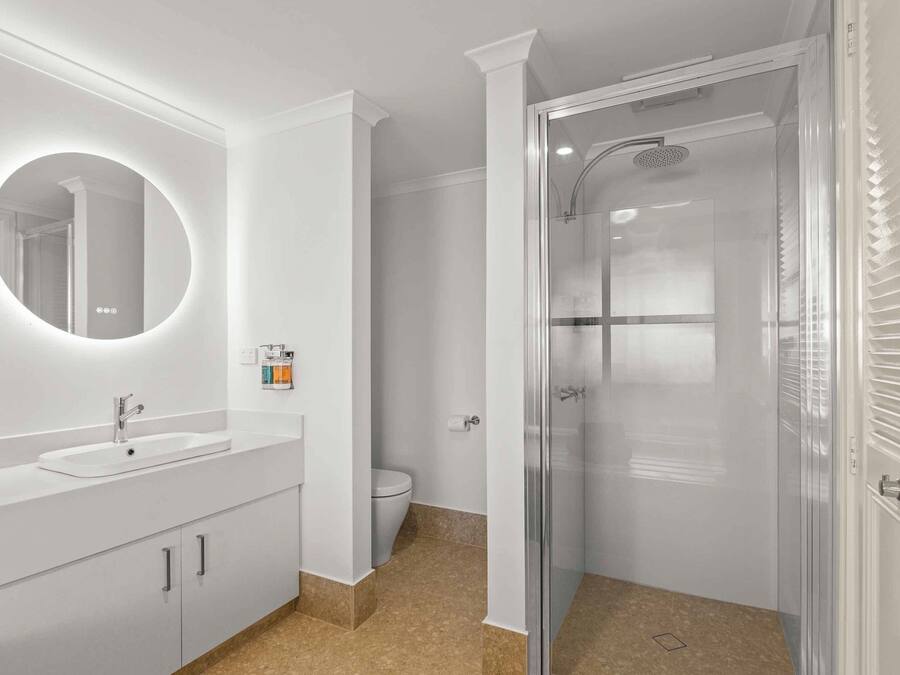 Un baño moderno con un espejo redondo, un lavamanos y una ducha con mampara de vidrio.
