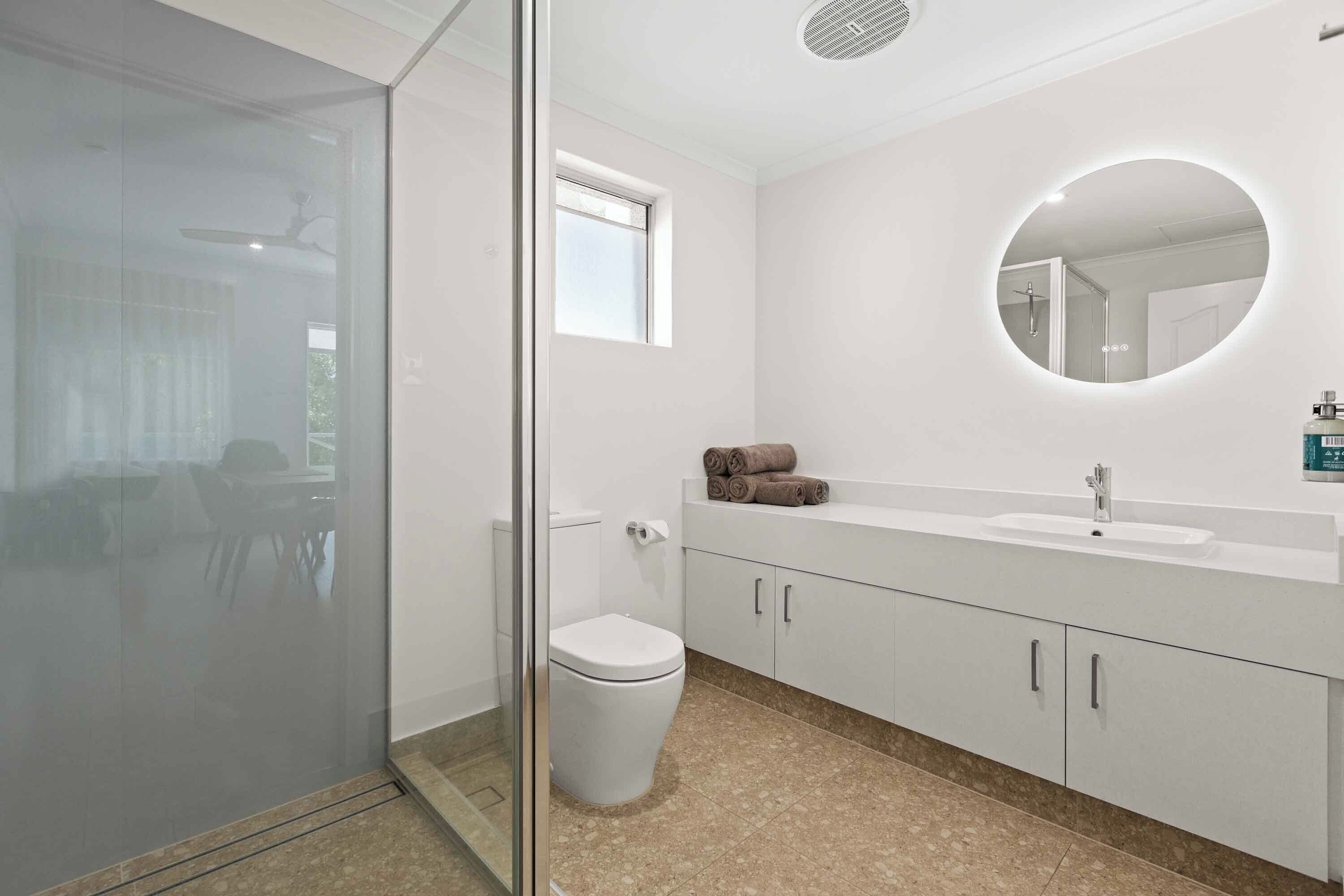 A modern bathroom with a glass shower enclosure, a toilet, a sink with a mirror, and a window.
