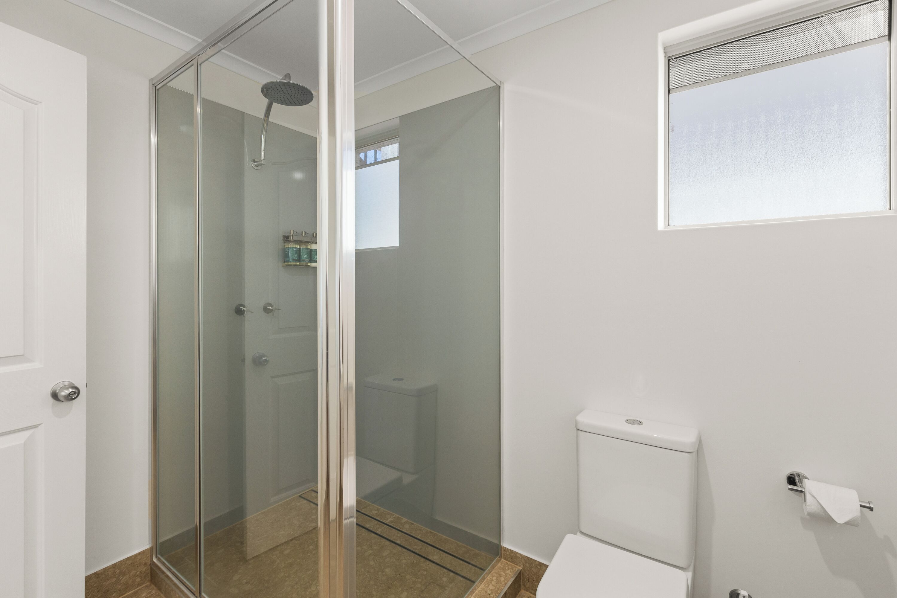 A bathroom with a glass-enclosed shower, a toilet, and a window.