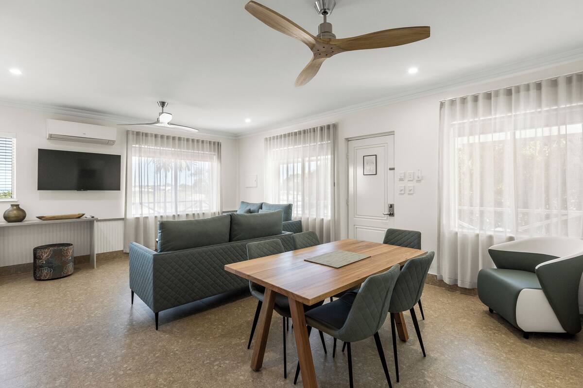 Una sala moderna con una mesa de comedor de madera, sofás verdes y un ventilador de techo.