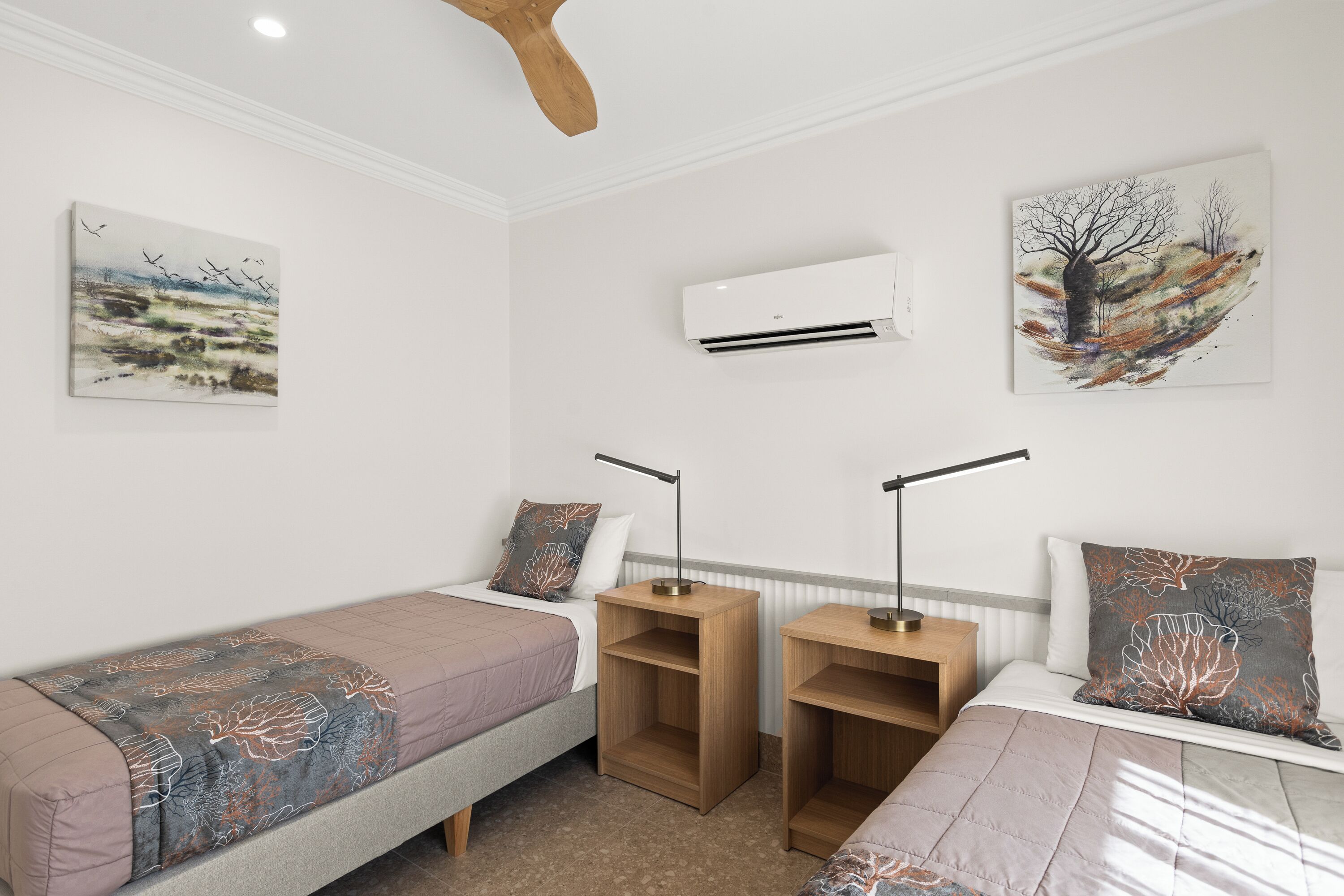 A bedroom with two single beds, a nightstand with a lamp, and artwork on the walls.
