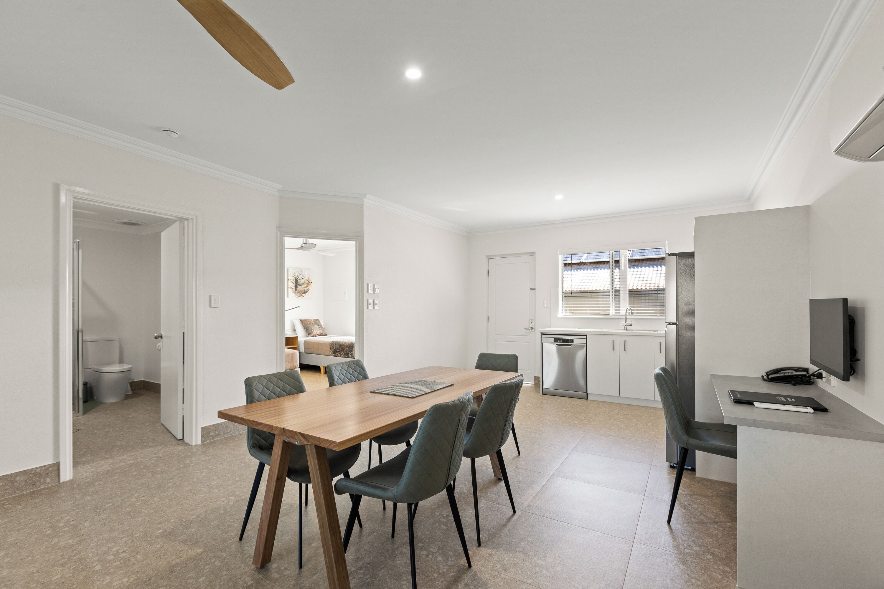 Une cuisine moderne avec des meubles blancs, un four encastré et un coin repas comprenant une table en bois et quatre chaises.