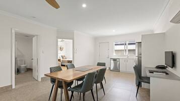 Une cuisine moderne avec des meubles blancs, un four encastré et un coin repas comprenant une table en bois et quatre chaises.