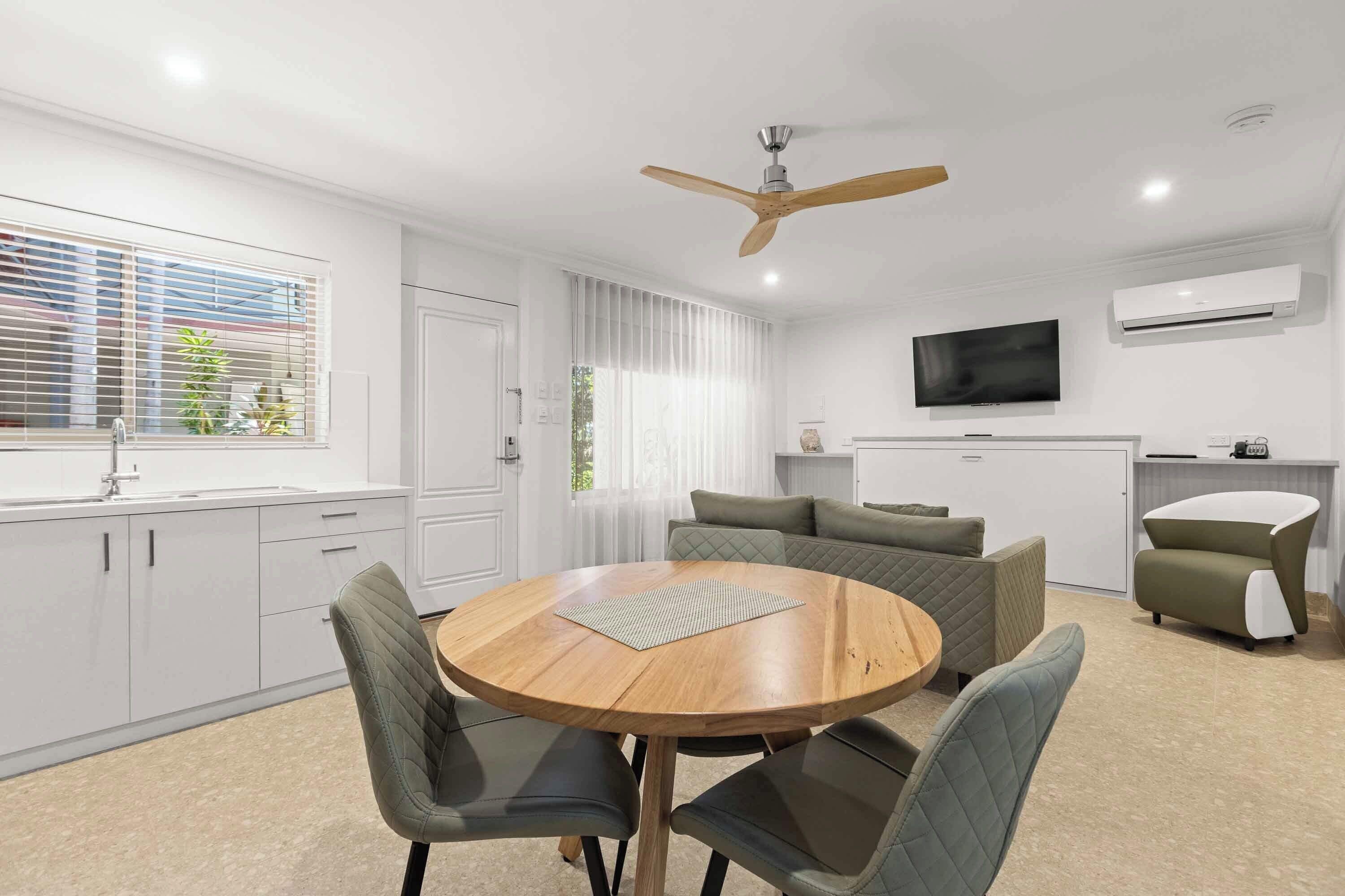 A modern kitchen with white cabinets, a round wooden table, and green upholstered chairs.