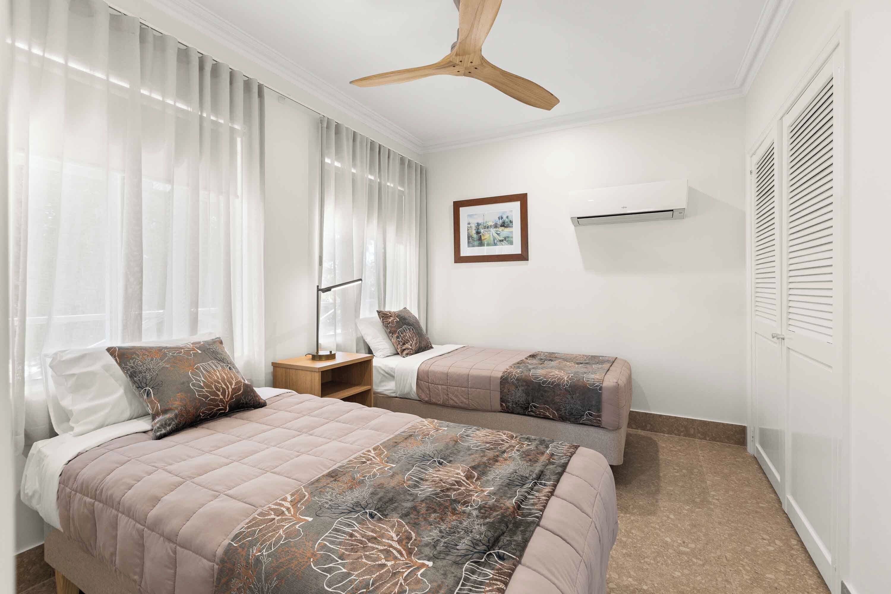 A bedroom with two beds, a ceiling fan, an air conditioning unit, and a framed picture on the wall.