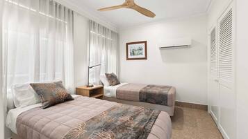 A bedroom with two beds, a ceiling fan, an air conditioning unit, and a framed picture on the wall.