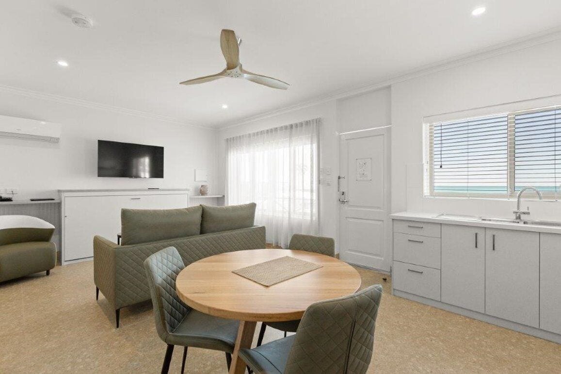 A modern kitchen with a round dining table, a ceiling fan, and a TV mounted on the wall.