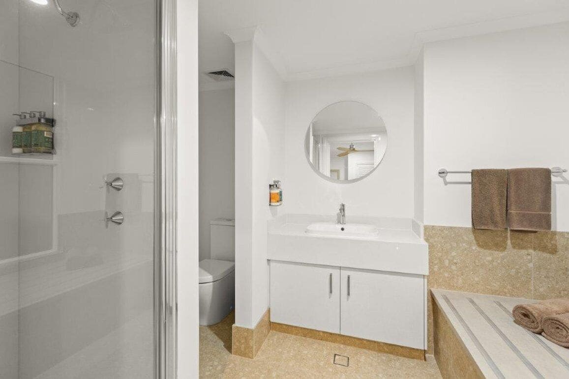 A bathroom with a glass shower enclosure, a white sink with a mirror above it, and a towel rack with towels.