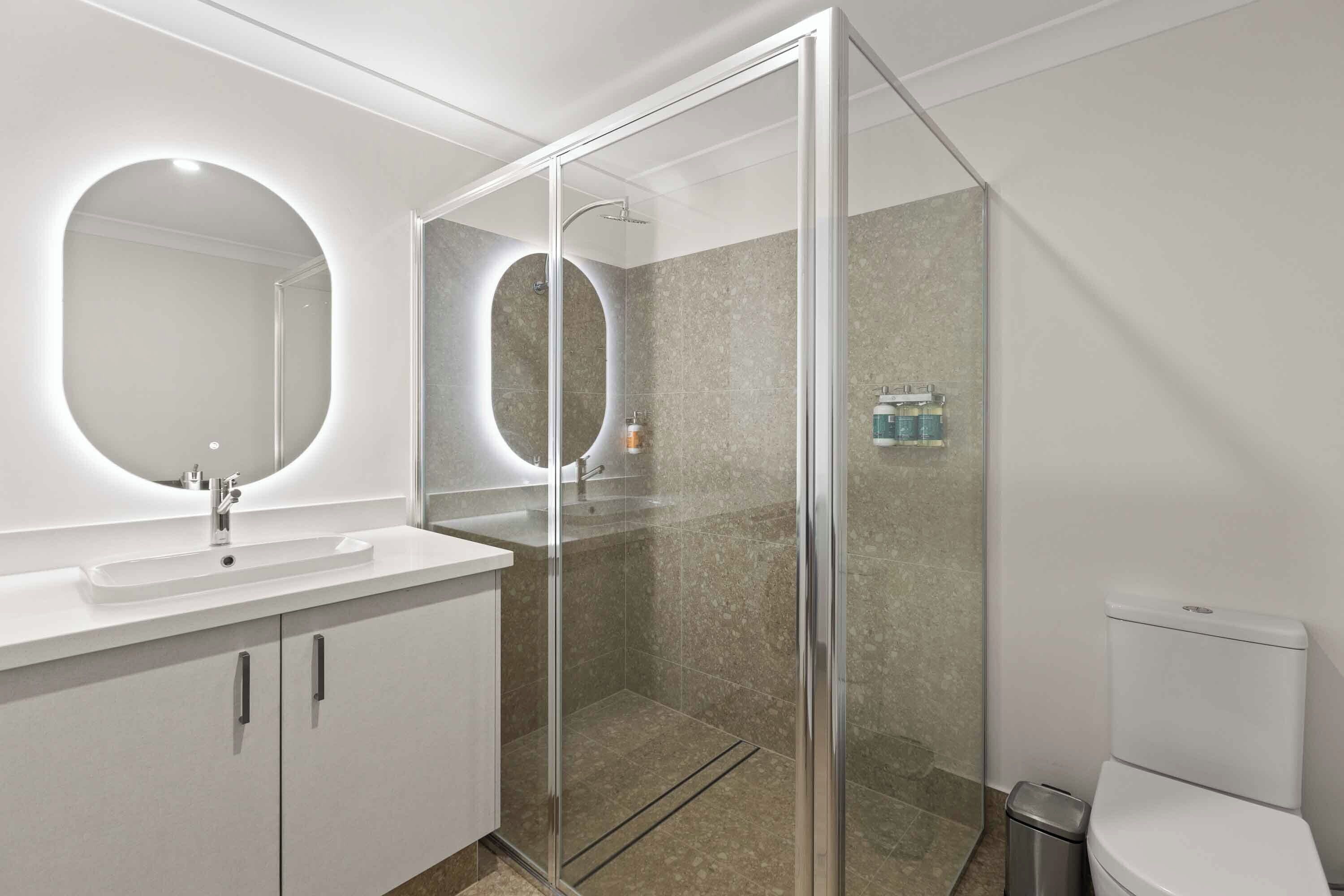 A modern bathroom with a glass-enclosed shower, a large mirror, and a white sink.