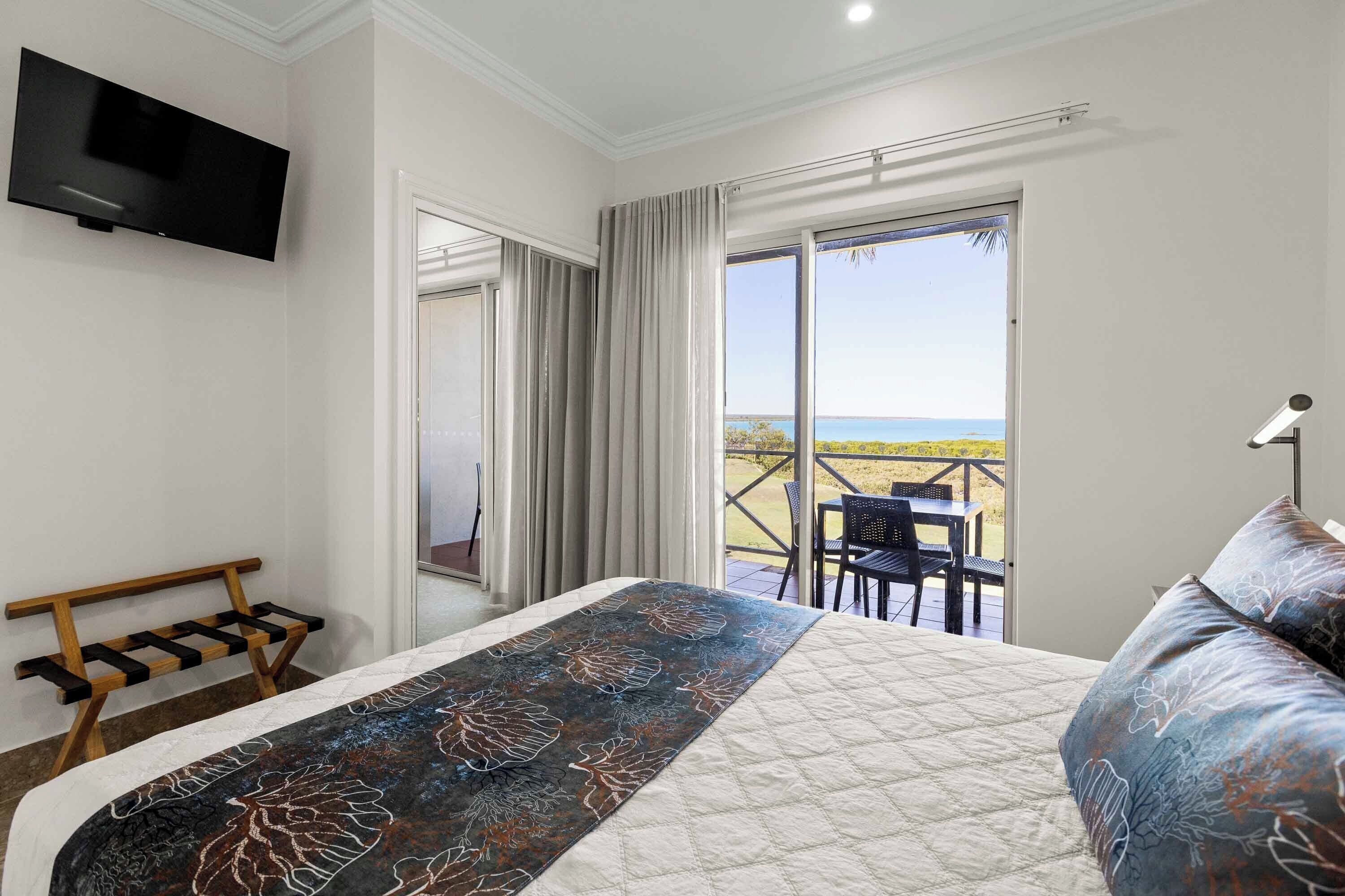 A bedroom with a bed, a TV, a bench, and a balcony with a view.