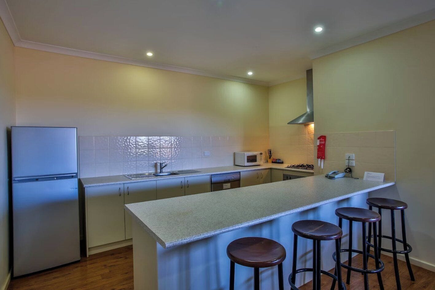 Cocina compacta con refrigerador, microondas, lavamanos y estufa a gas pequeña. Hay tres taburetes en la isla.