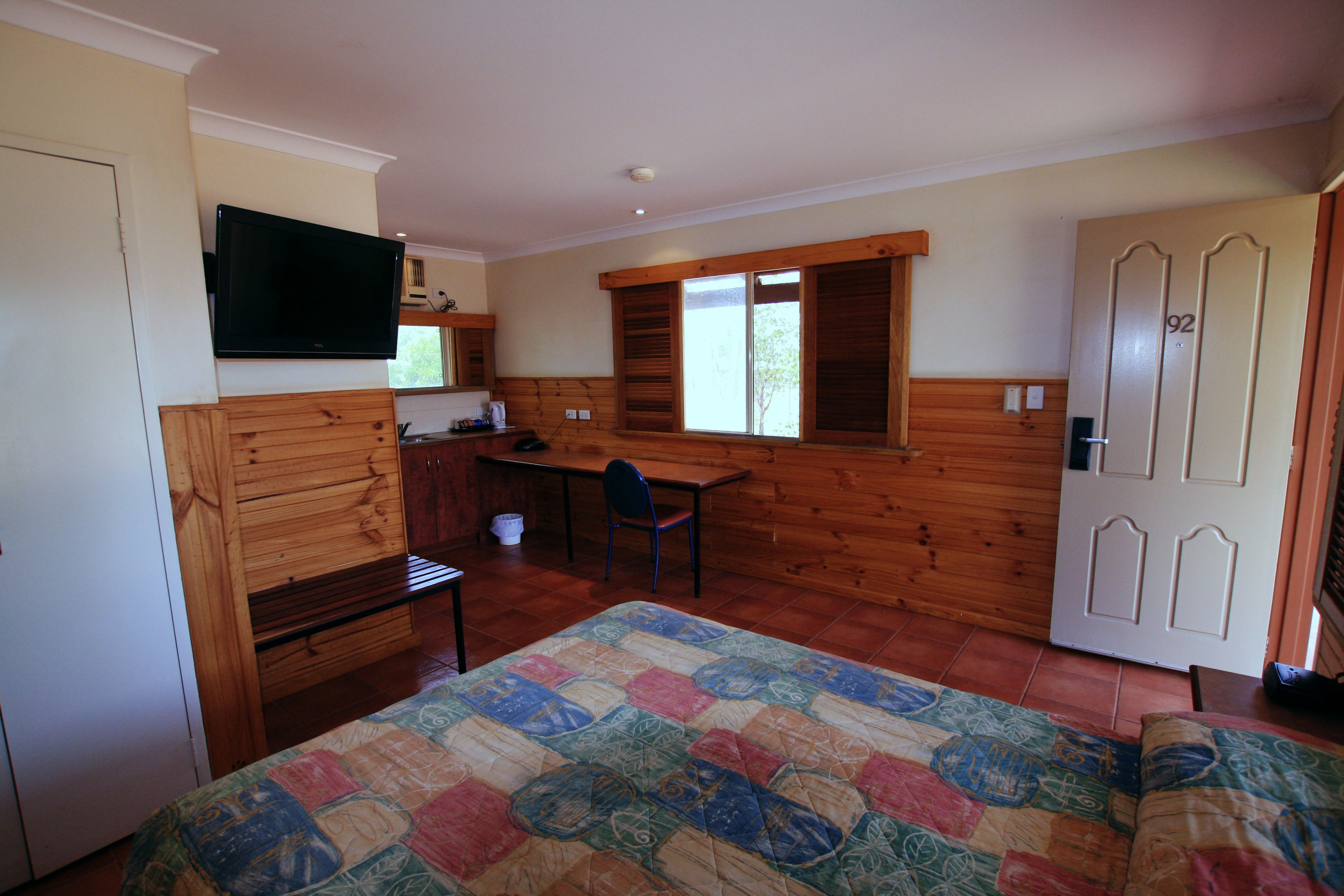 Una habitación con una cama, un escritorio, una silla, un televisor y una puerta con un número.