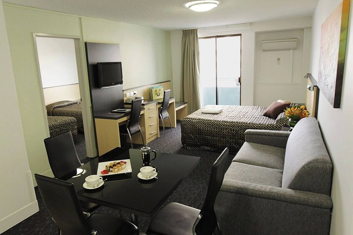 Habitación de hotel con mesa de comedor, sillas, sofá, cama, televisión y balcón con vistas.