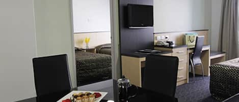 A hotel room with a bed, a desk with a computer, a chair, a coffee machine, and a breakfast tray.