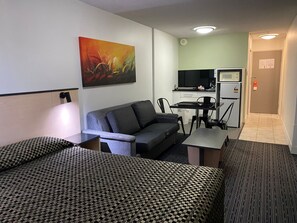 Habitación de hotel con dos camas, un sofá, un escritorio, una silla, un televisor y una kitchenette.