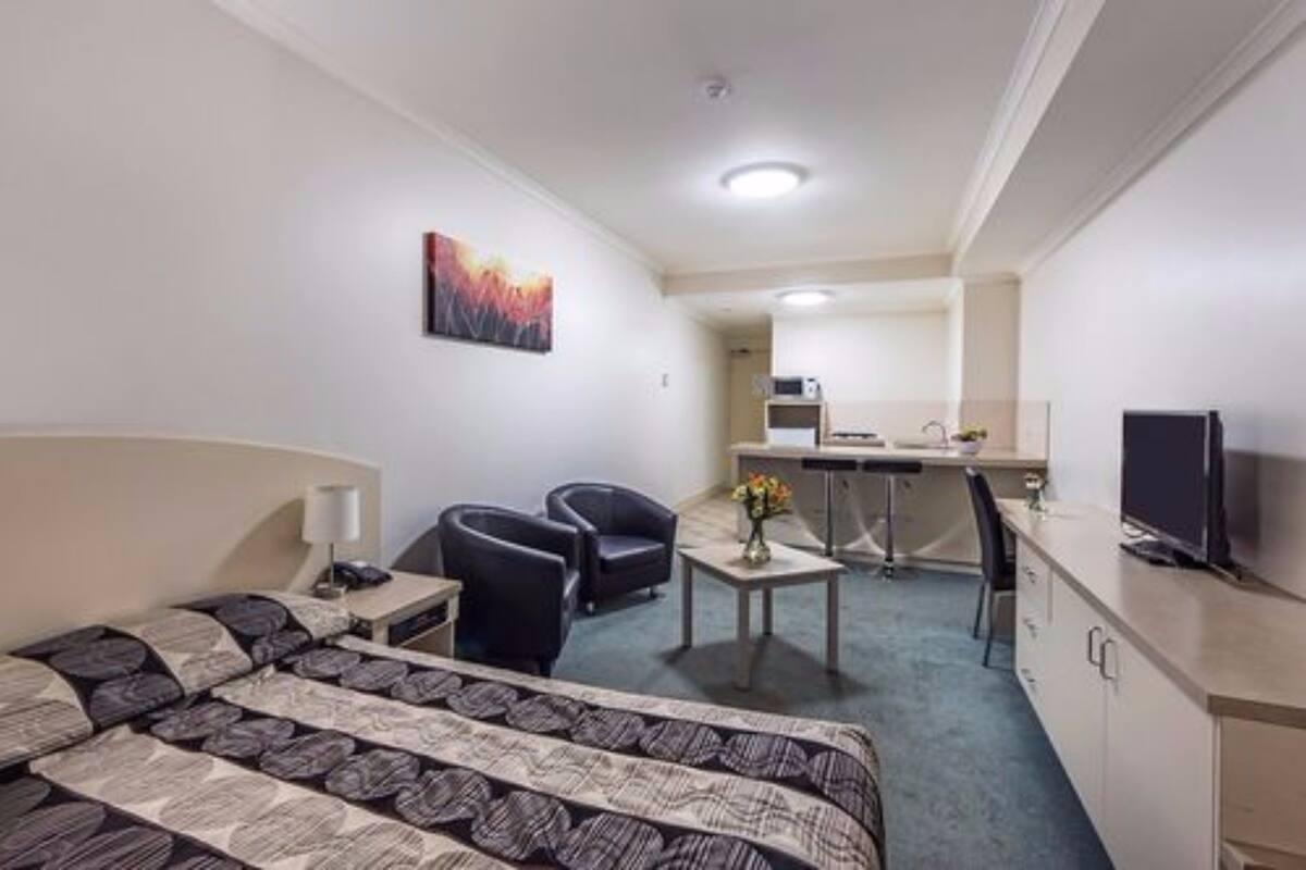 Habitación de hotel con cama, dos sillones, un escritorio con computadora, un televisor y un cuadro en la pared.