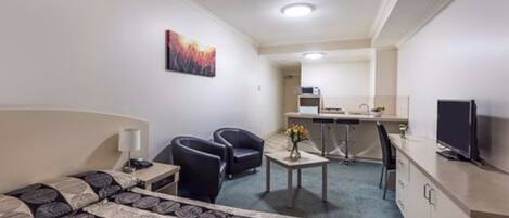 A hotel room with a bed, two chairs, a desk with a computer, a TV, and a painting on the wall.