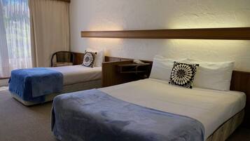 A hotel room with two beds, a desk with a phone, and a window with curtains.