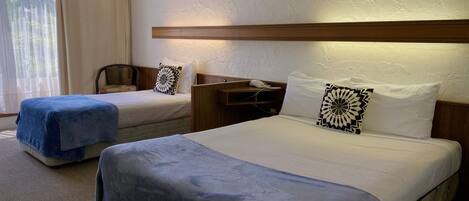 A hotel room with two beds, a desk with a phone, and a window with curtains.