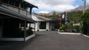 A building with a covered outdoor area, a parking lot, and a mountainous backdrop. - West Coaster Motel (Queenstown)