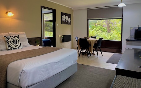 A hotel room with a bed, a desk, and a view of greenery.