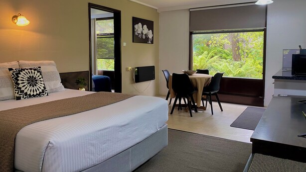 A hotel room with a bed, a desk, and a view of greenery. - West Coaster Motel (Queenstown)