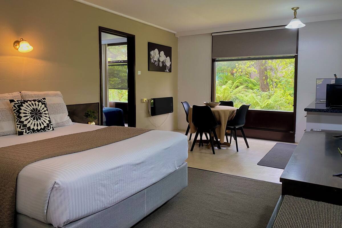 A hotel room with a bed, a desk, and a view of greenery.