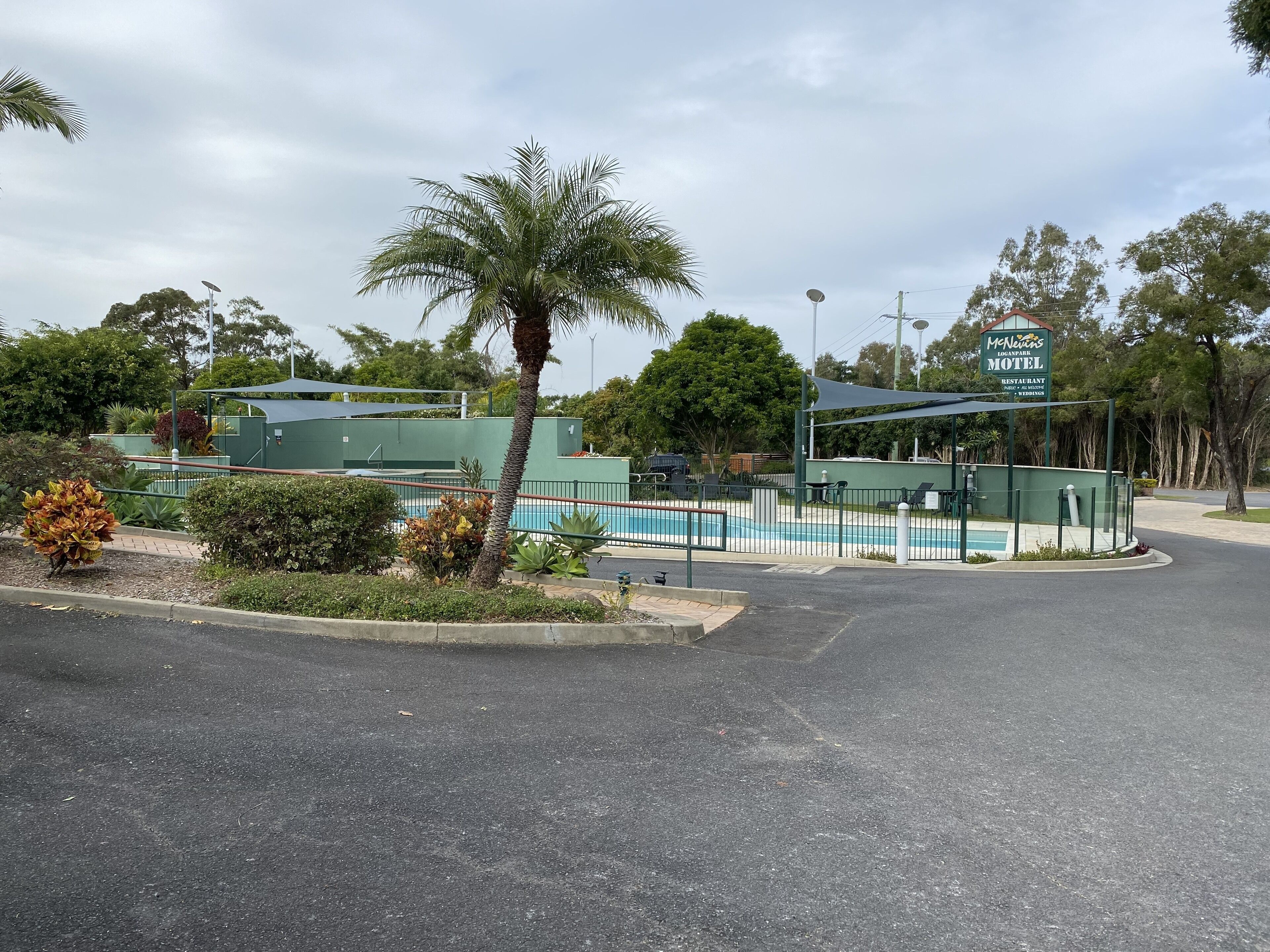 A motel with a pool, surrounded by greenery and a palm tree.