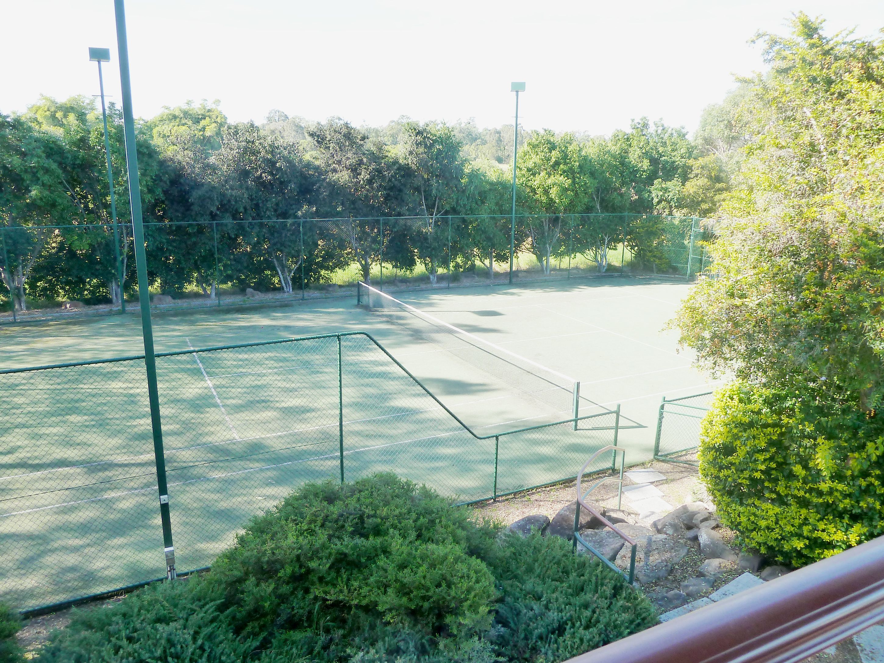 An outdoor tennis court surrounded by trees and greenery.