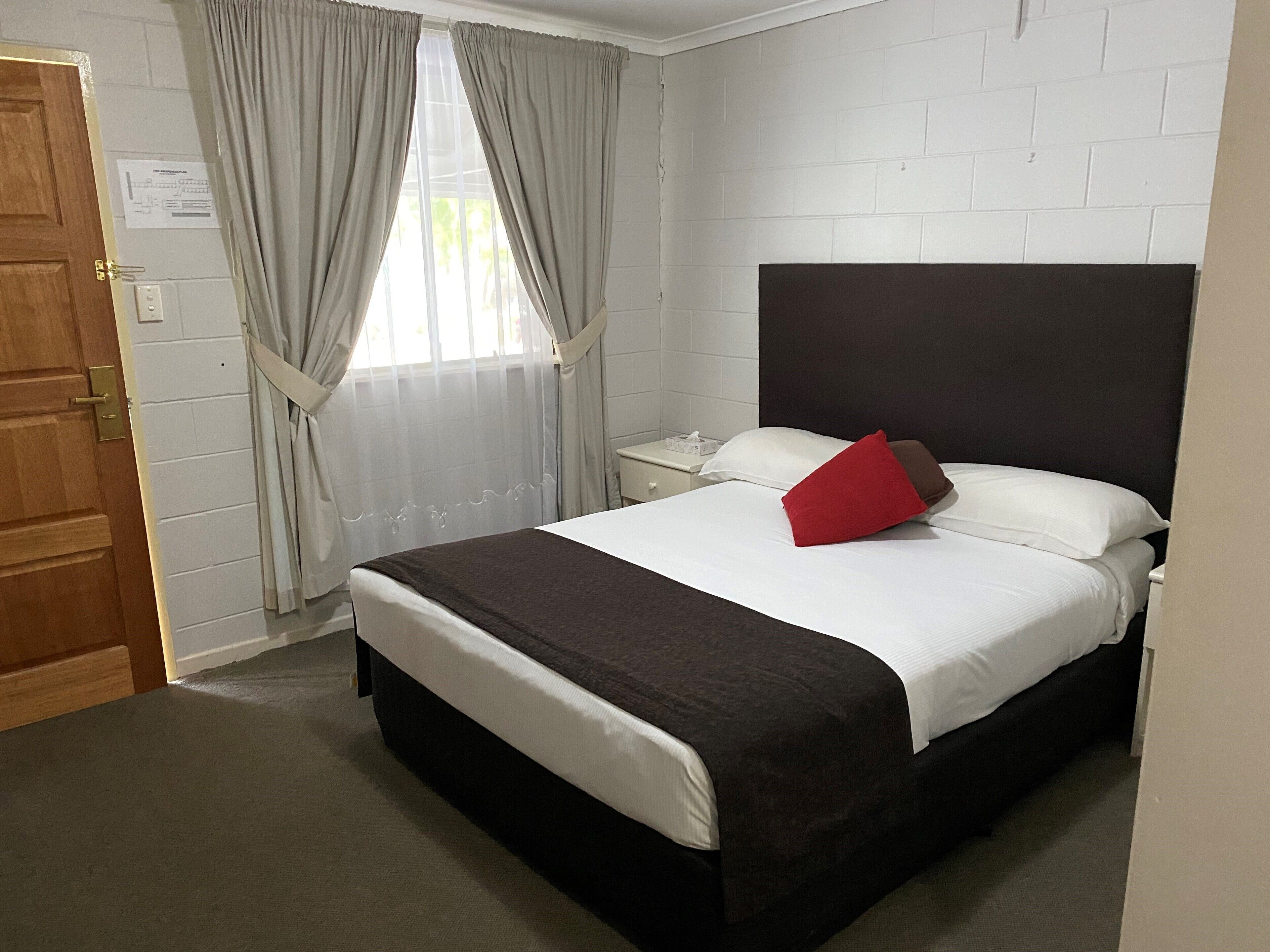 A hotel room with a bed, a nightstand, a window with curtains, and a door.