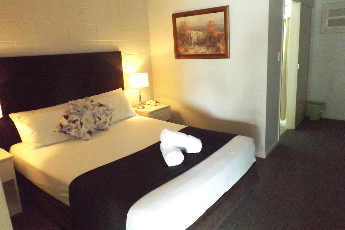 A neatly made bed with a pillow, a bedside lamp, and a painting on the wall.
