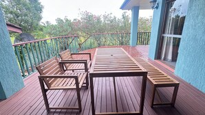 Una terraza de madera con una mesa, sillas, barandilla y vista a la vegetación.