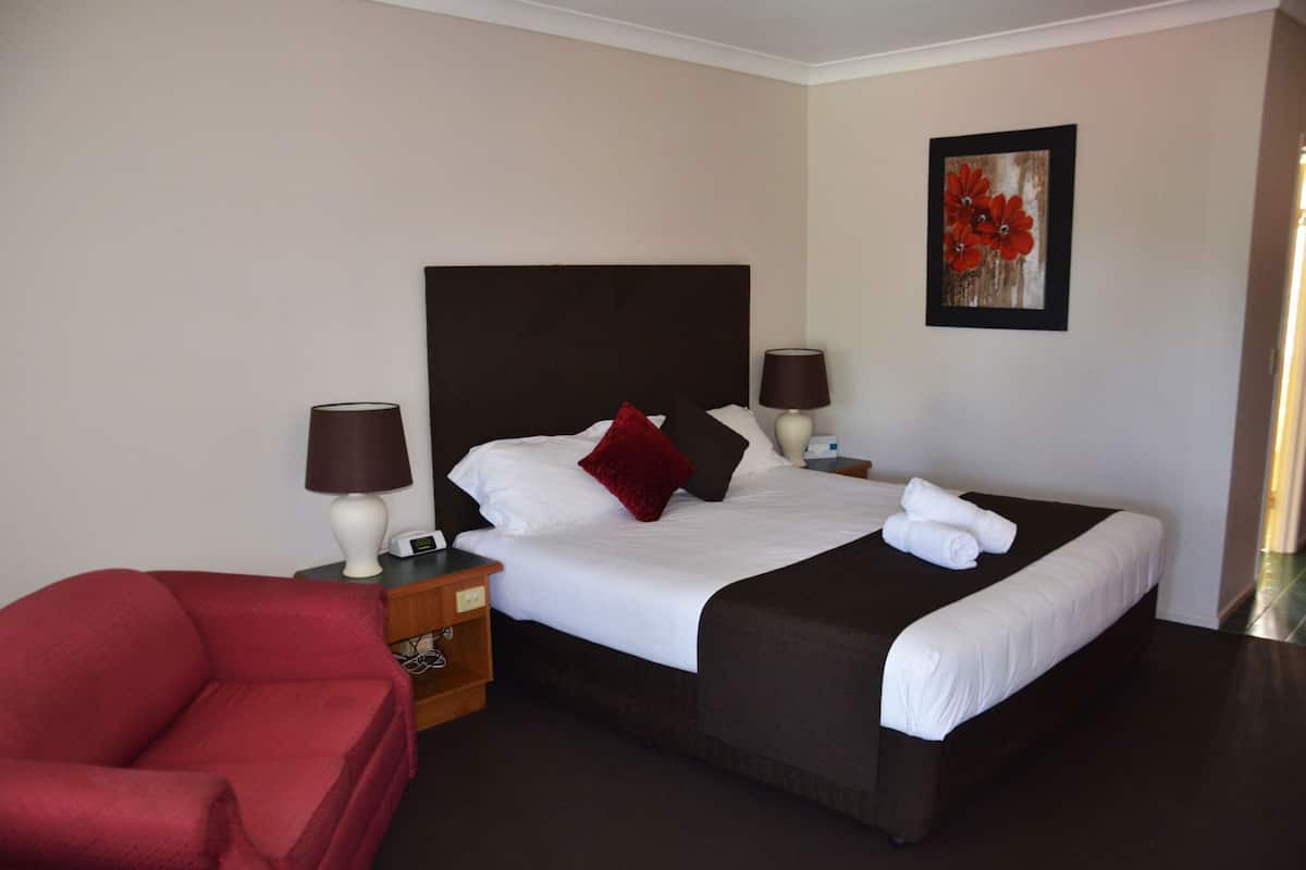 A hotel room with a bed, two bedside lamps, a red chair, a painting, and a nightstand with a phone.