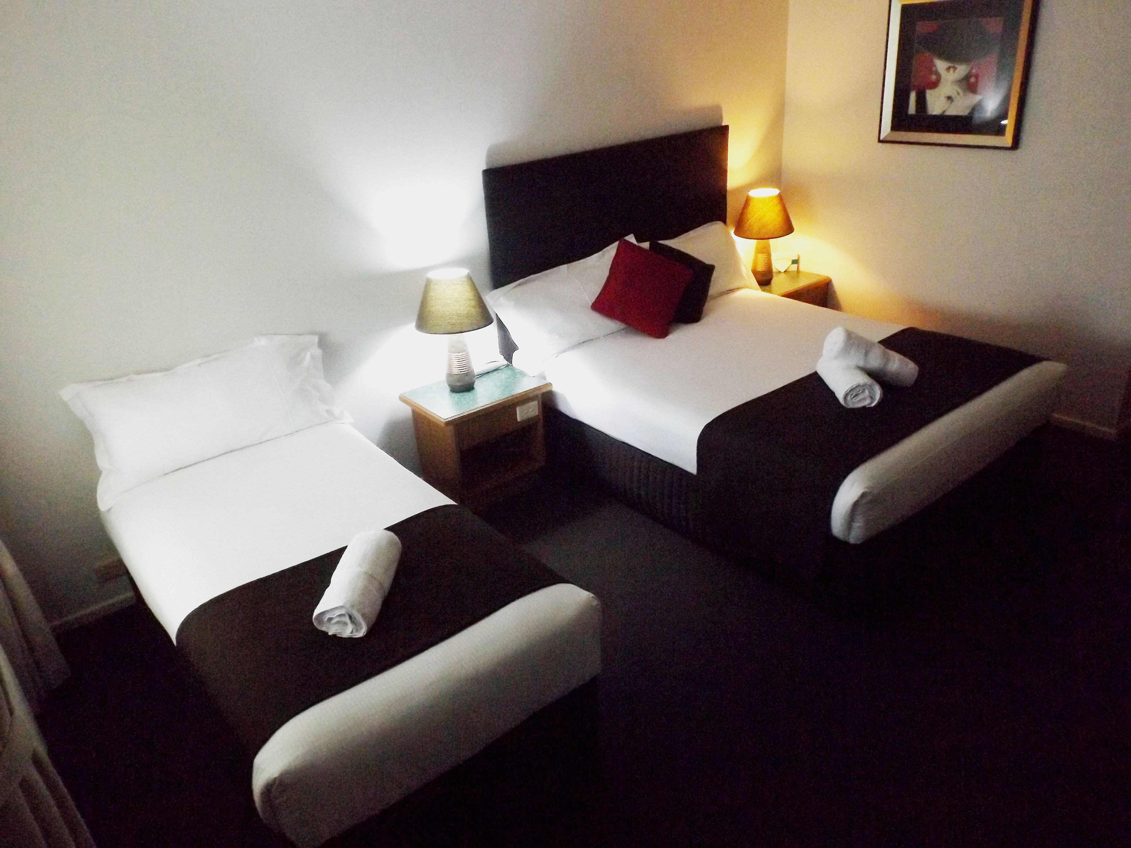 A hotel room with two single beds, a nightstand with a lamp, and a framed picture on the wall.