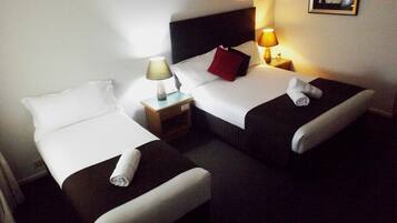 A hotel room with two single beds, a nightstand with a lamp, and a framed picture on the wall.