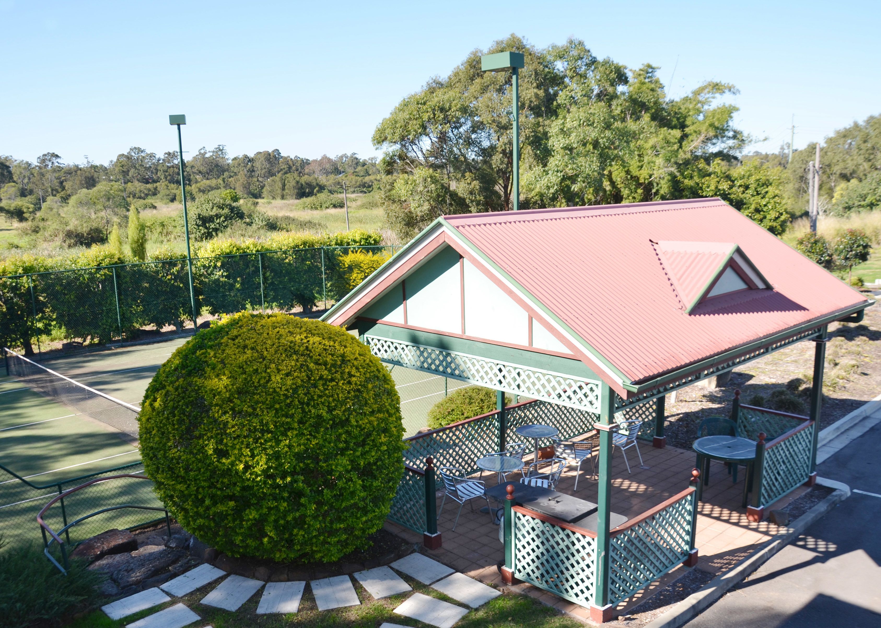 A pavilion with a red roof, surrounded by a green fence, and a neatly trimmed bush in the foreground.