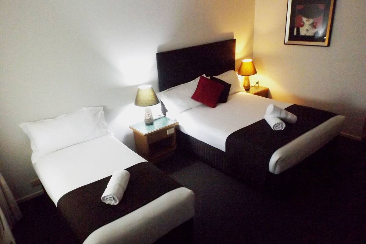 A hotel room with two single beds, a nightstand with a lamp, and a framed picture on the wall.