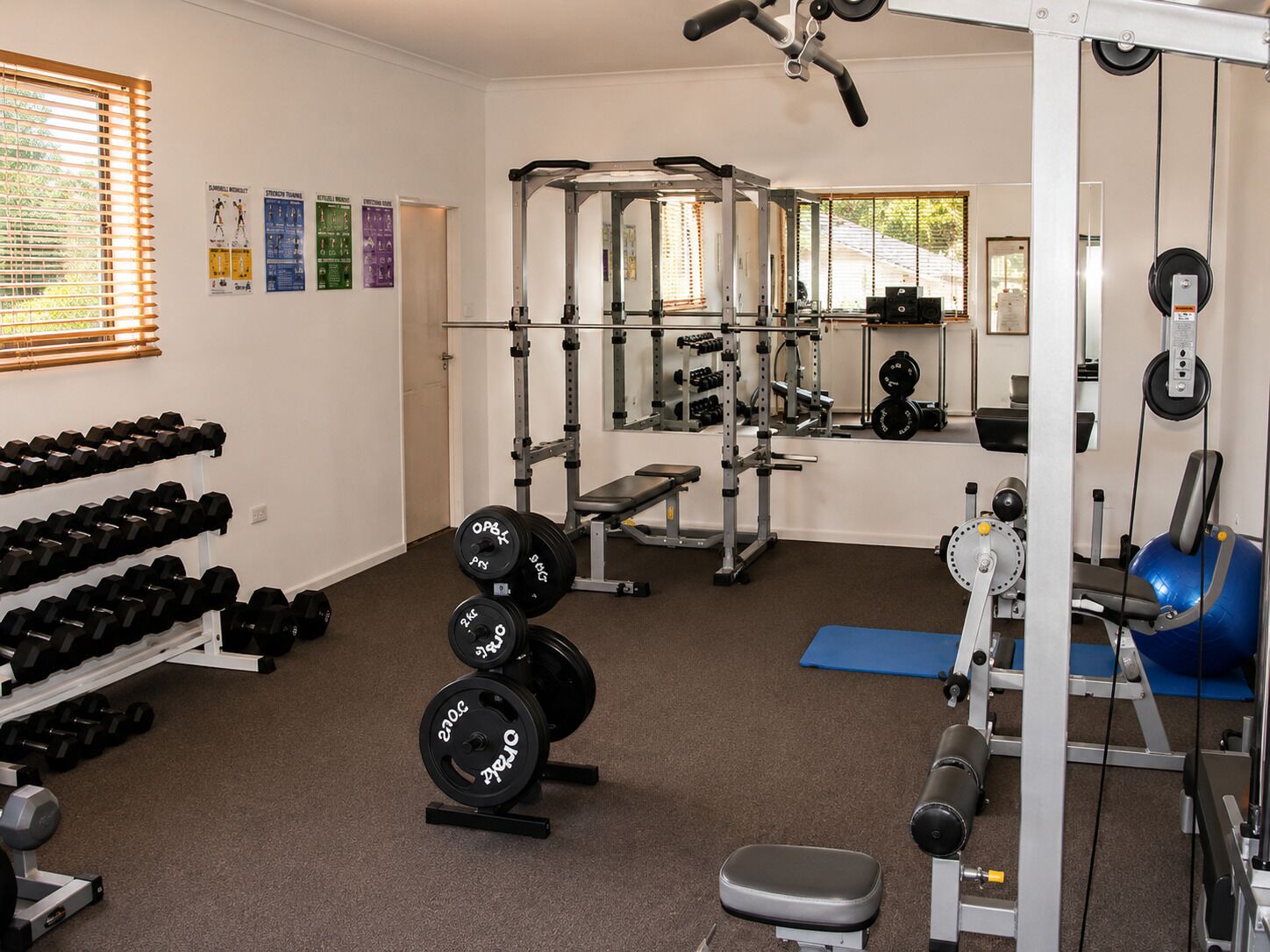 Un gimnasio con equipamiento de levantamiento de pesas, mancuernas y máquinas de ejercicio.