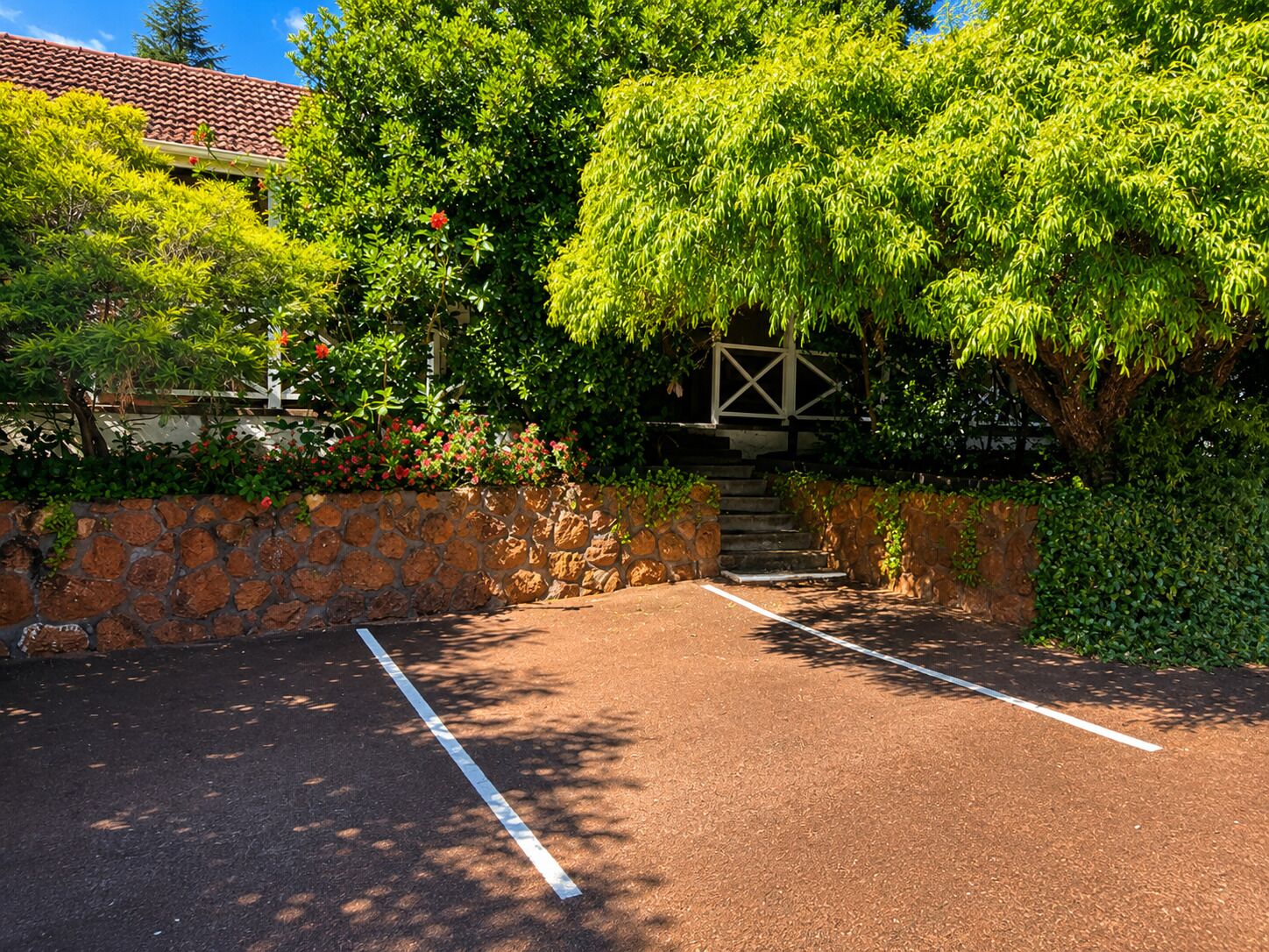 A paved parking area with a stone wall and a staircase leading to a covered walkway.