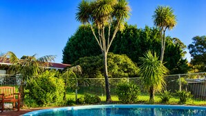 A swimming pool surrounded by lush greenery and a metal fence. - Karri Forest Motel (Pemberton)