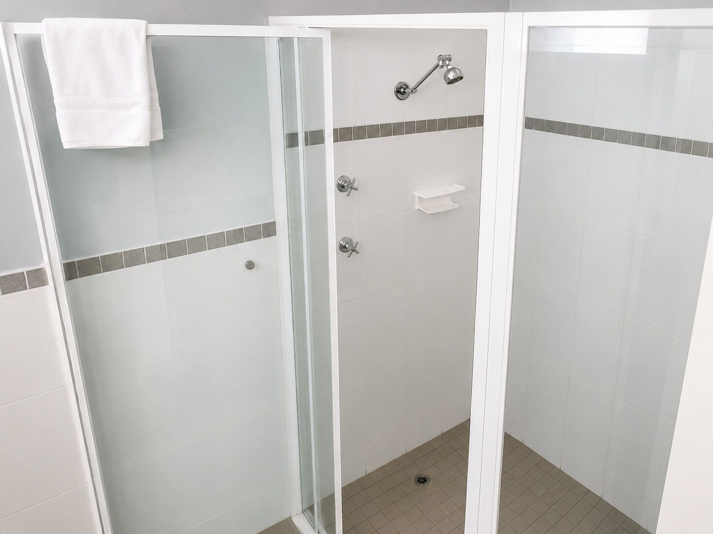 Un box de ducha con paredes de vidrio, una toalla blanca colgada en la puerta, un cabezal de ducha y un estante pequeño.