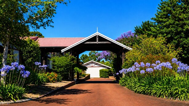 A pathway leading to a building with a red roof, surrounded by lush greenery and purple flowers. - Karri Forest Motel (Pemberton)