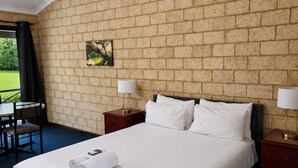 A hotel room with a brick wall, a bed with white linens, a ceiling fan, a nightstand with a lamp, and a window with a view. - Karri Forest Motel (Pemberton)